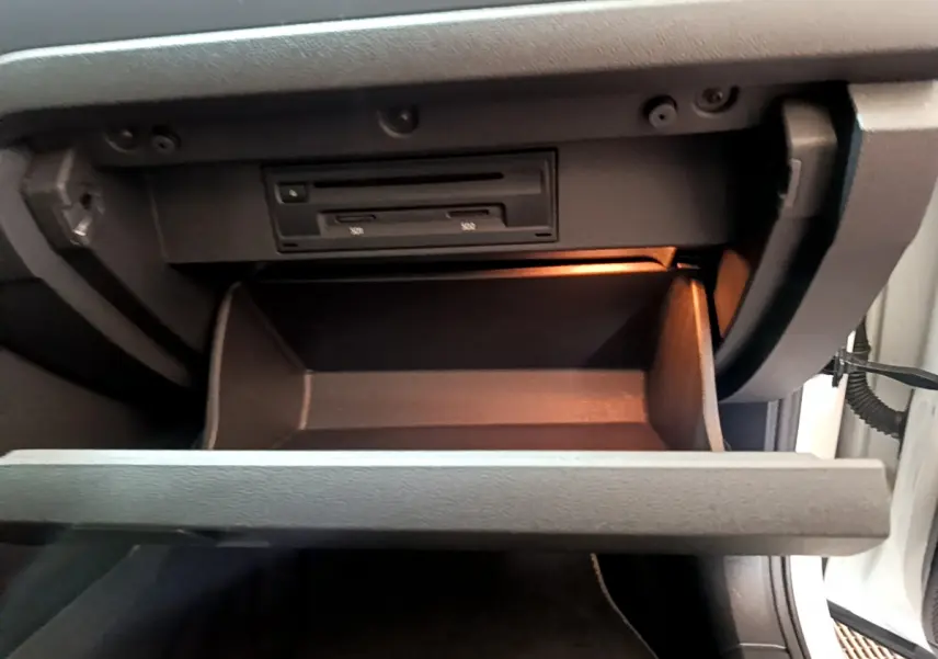 Vue rapprochée de la boîte à gants ouverte du Volkswagen T-Roc blanc, éclairage intérieur orange visible.