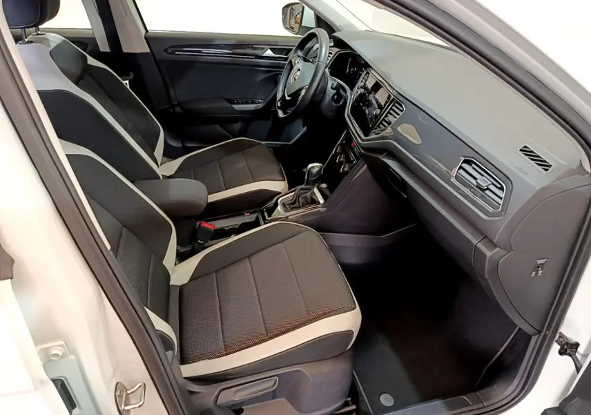 Intérieur du Volkswagen T-Roc blanc vu côté conducteur, sièges bi-ton noirs et gris, tableau de bord moderne avec écran tactile.