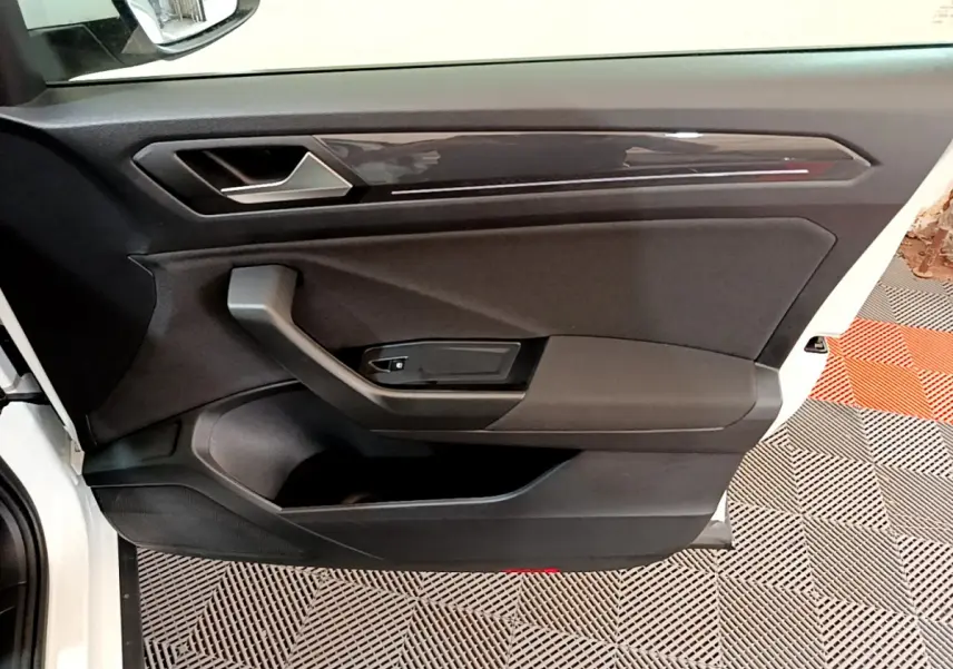 Intérieur côté conducteur de la porte d'une Volkswagen T-Roc blanche, avec poignée et panneau noir mat.