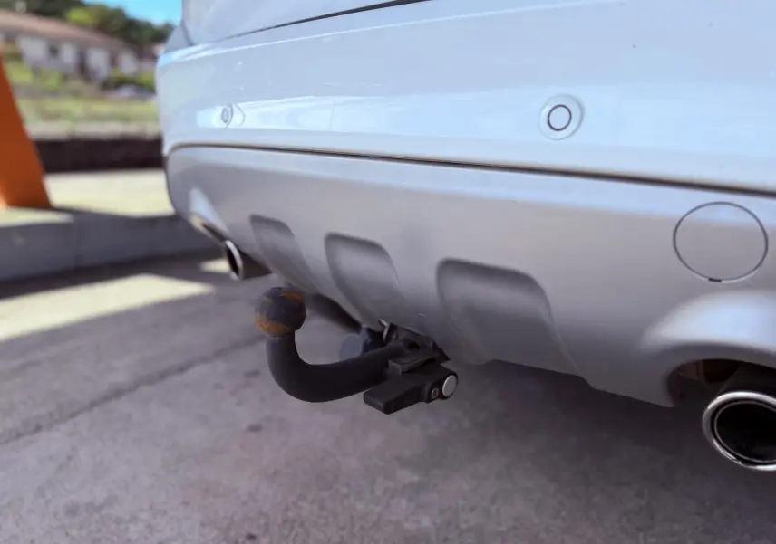 Gros plan sur l'attelage arrière rouillé d'un Ford Kuga blanc, avec pare-chocs et sortie d'échappement visibles.