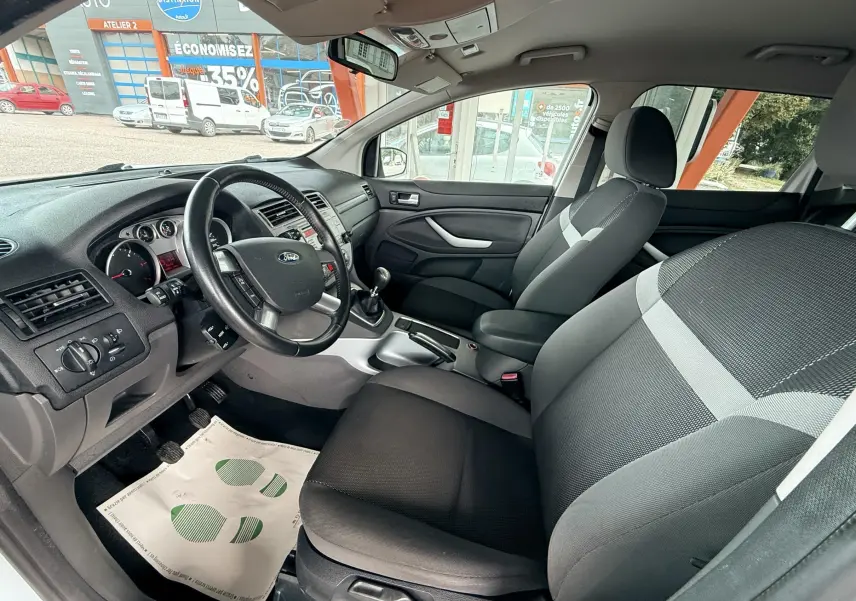 Intérieur avant du Ford Kuga blanc 2012, vue côté conducteur montrant tableau de bord et sièges tissu gris noir.