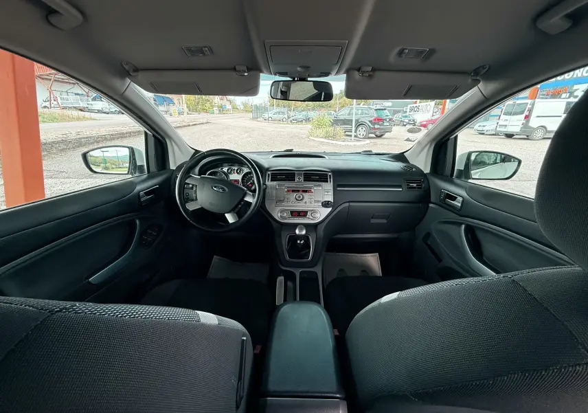 Intérieur avant d'une Ford Kuga blanc 2012, vue du tableau de bord et volant côté gauche avec sièges tissu gris noir.