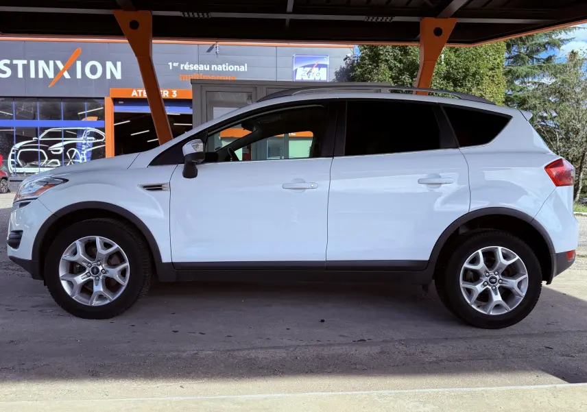 Ford Kuga blanc vu de profil côté gauche sous un abri avec jantes alliage et vitres teintées.