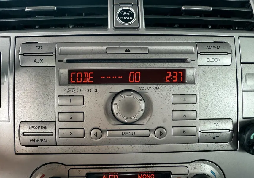 Gros plan sur la console centrale du Ford Kuga blanc de 2012, affichant l'autoradio 6000 CD et la climatisation digitale.