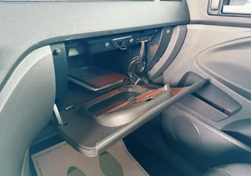 Gros plan sur la boîte à gants ouverte côté passager du Ford Kuga 2012 avec intérieur gris et câbles visibles.