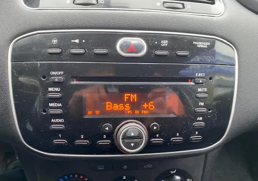 Gros plan sur la console centrale de la Fiat Grande Punto 2015, affichant l'autoradio FM avec réglage des basses à +6.