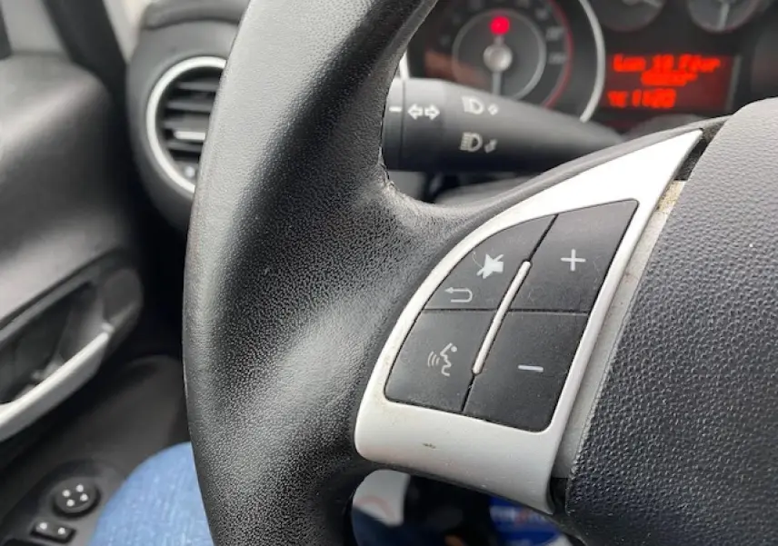 Gros plan sur les commandes au volant noir de la Fiat Grande Punto gris, avec tableau de bord et aérateur en arrière-plan.