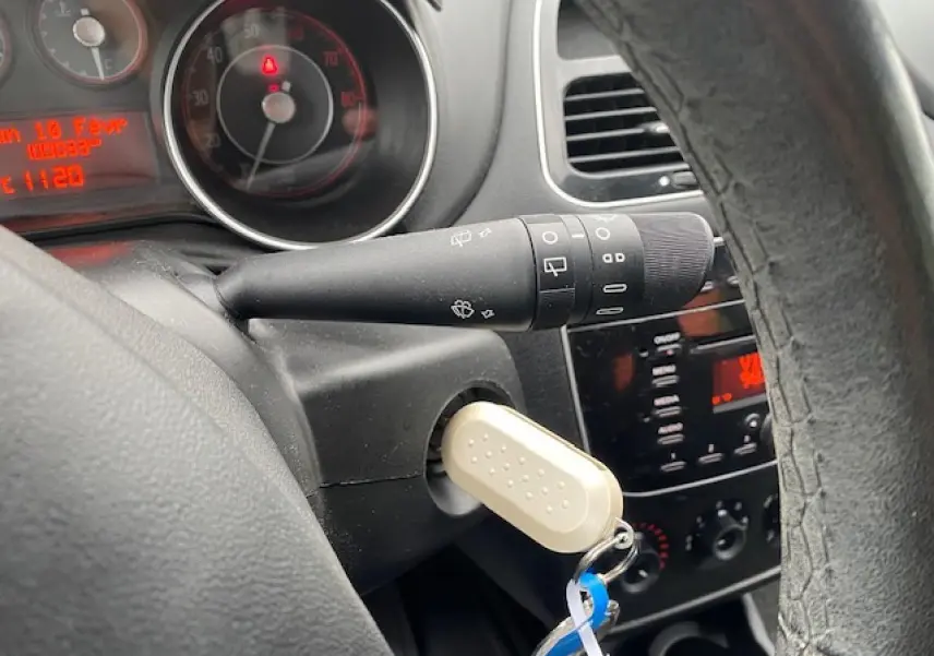 Vue rapprochée du tableau de bord et du volant d'une Fiat Grande Punto gris, avec clé insérée et commandes visibles.