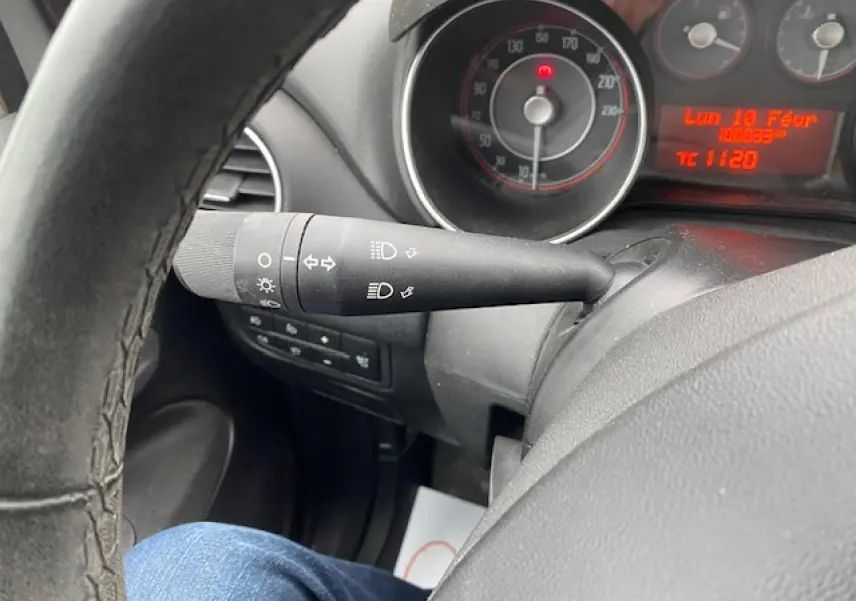 Gros plan sur le commodo des feux et le tableau de bord du Fiat Grande Punto gris, avec compteur et affichage digital rouge.