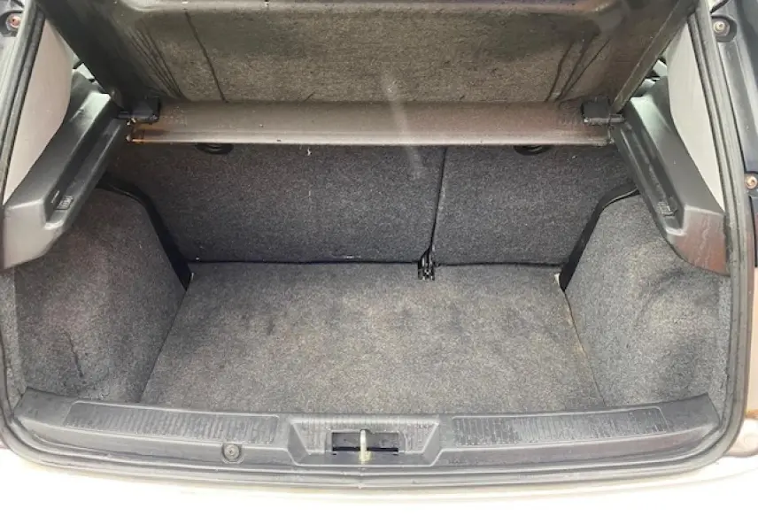 Coffre ouvert de la Fiat Grande Punto gris, vue de l'arrière montrant l'espace de chargement vide et la moquette intérieure.