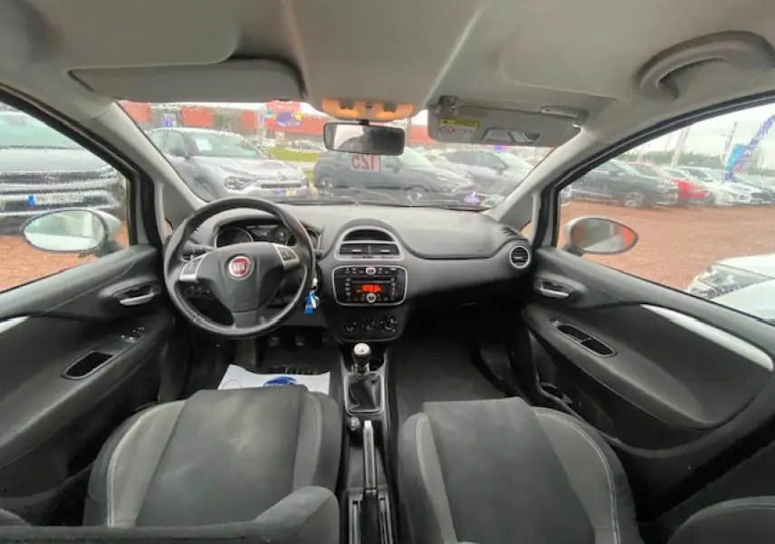 Intérieur noir de la Fiat Grande Punto 2015, vue frontale du tableau de bord avec volant multifonction et boîte manuelle.