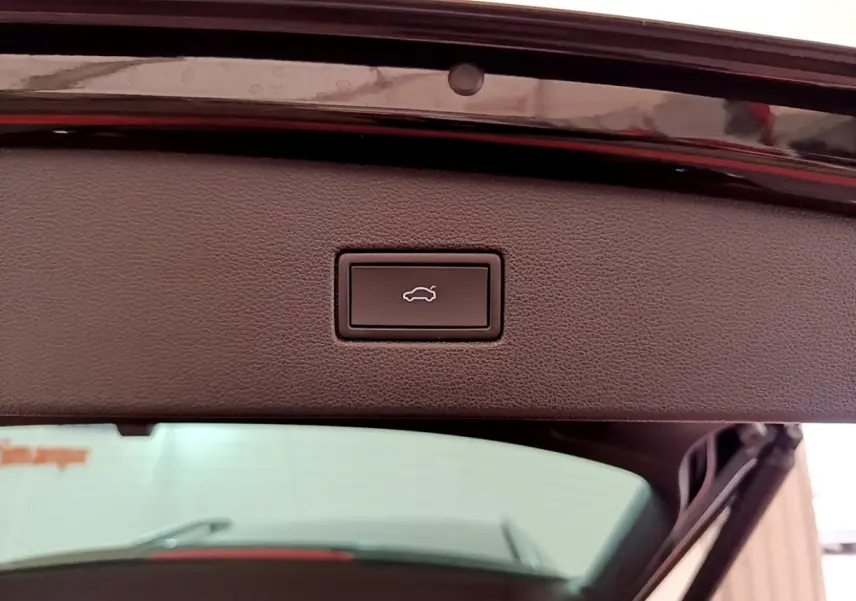 Bouton d'ouverture électrique du coffre sur la partie intérieure du hayon d'un Volkswagen Tiguan noir, vue en gros plan.