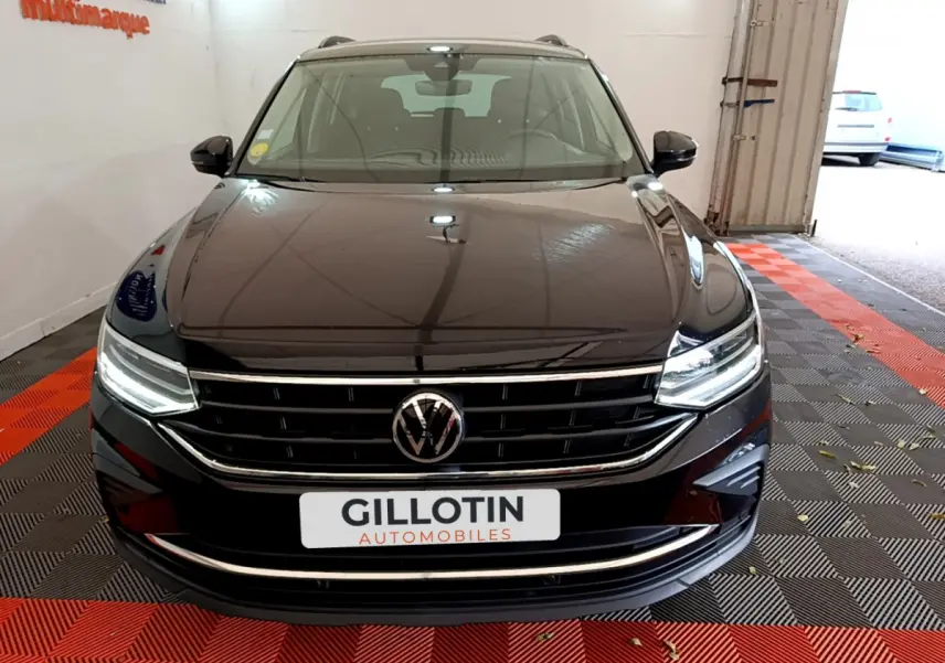 Vue frontale d'un Volkswagen Tiguan noir avec calandre chromée et phares LED allumés dans un garage.