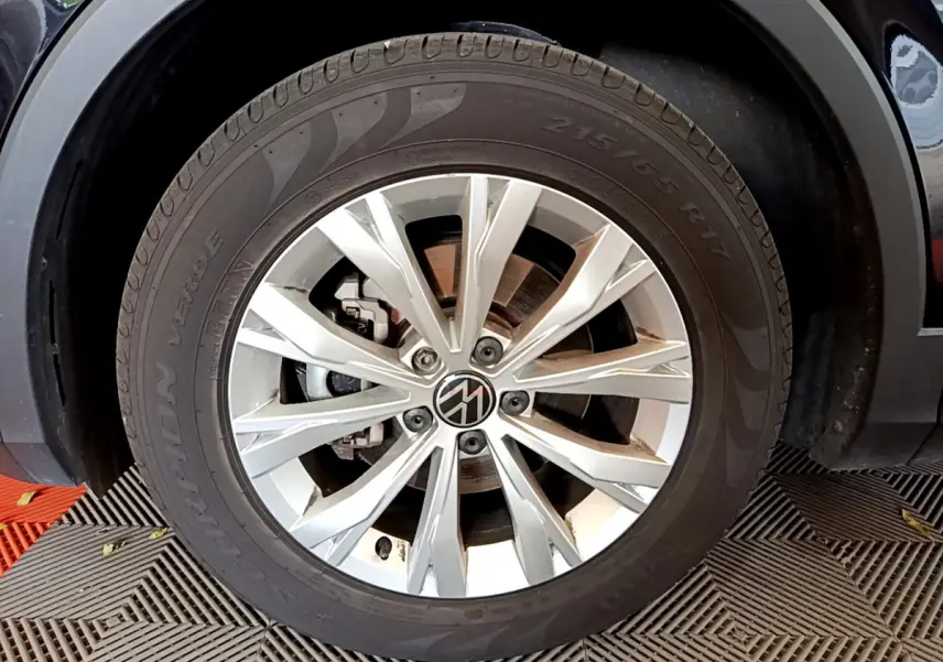 Gros plan sur la roue avant droite du Volkswagen Tiguan noir, avec jante alliage argentée et logo VW central.