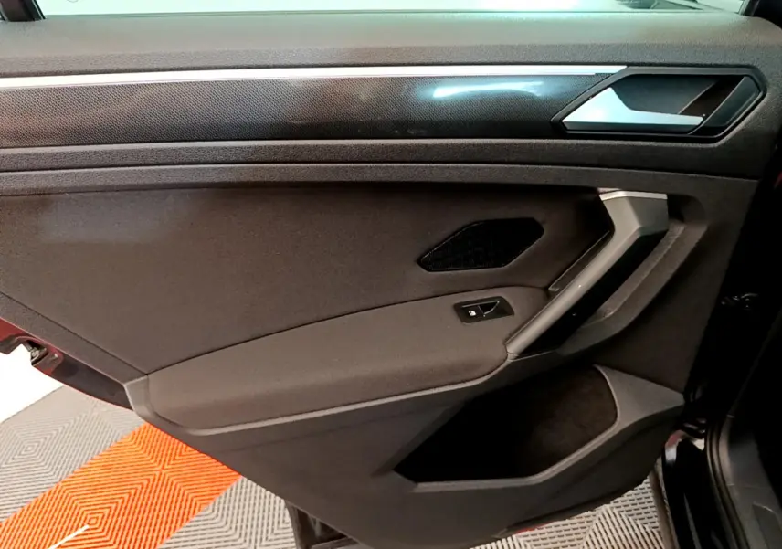 Porte intérieure côté gauche noire du Volkswagen Tiguan 2021 avec poignée argentée et bouton de verrouillage.