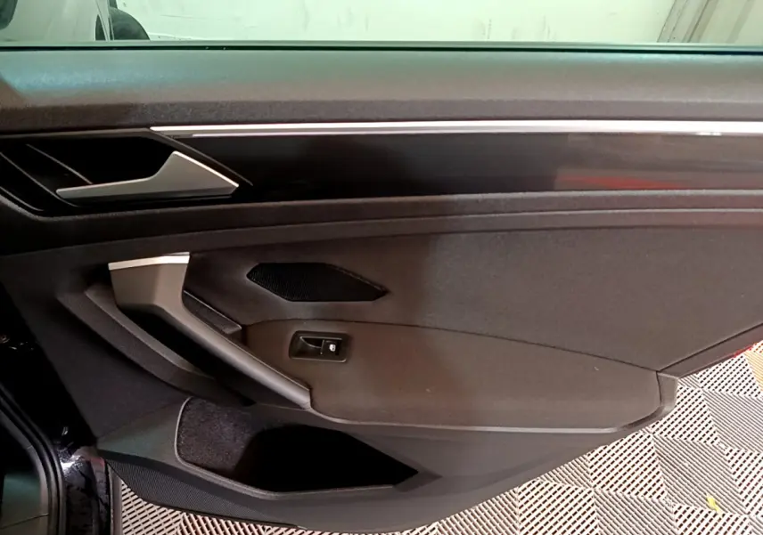 Détail de la porte côté gauche noire du Volkswagen Tiguan 2.0 TDI 150 DSG7 avec poignée argentée et haut-parleur intégré.