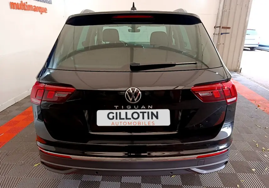 Vue arrière d'un Volkswagen Tiguan noir 2021 avec feux LED et logo central visible dans un garage.