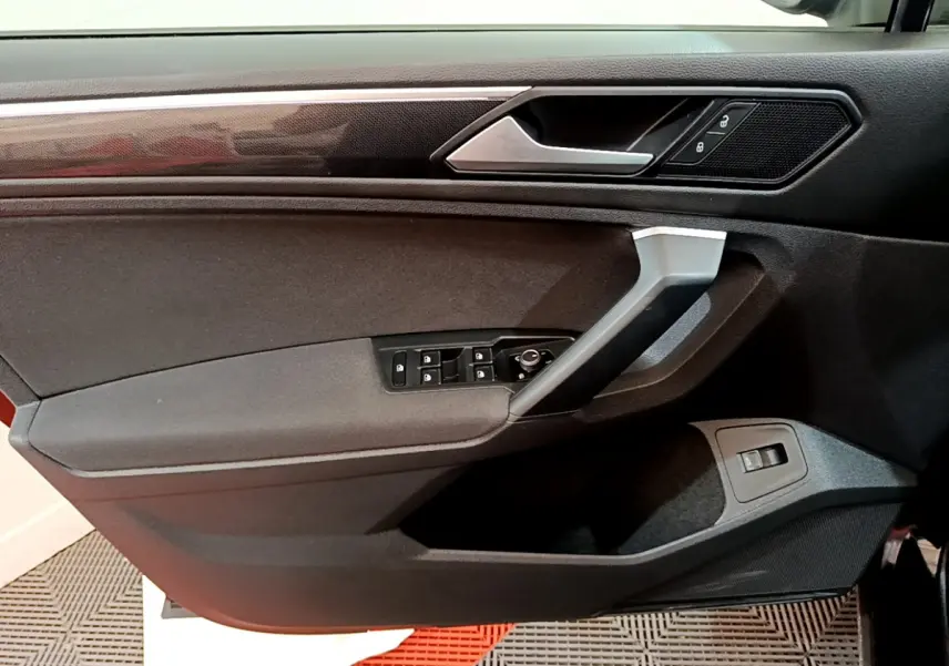 Détail de la porte côté gauche du Volkswagen Tiguan noir 2021 avec commandes électriques et poignée argentée.
