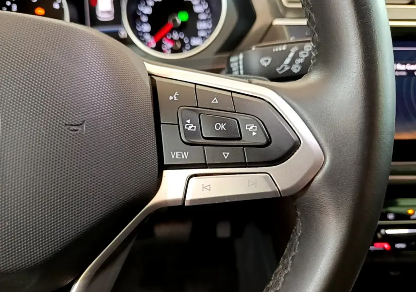 Gros plan sur les commandes au volant côté droit du Volkswagen Tiguan 2.0 TDI noir, avec tableau de bord lumineux en arrière-plan.
