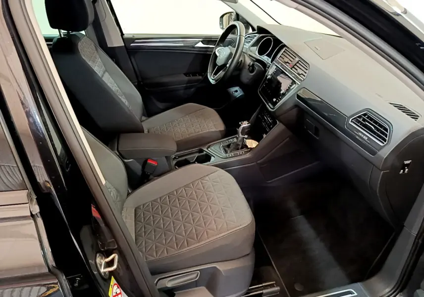 Intérieur avant droit du Volkswagen Tiguan noir 2021, sièges tissu gris avec motif géométrique et tableau de bord moderne.