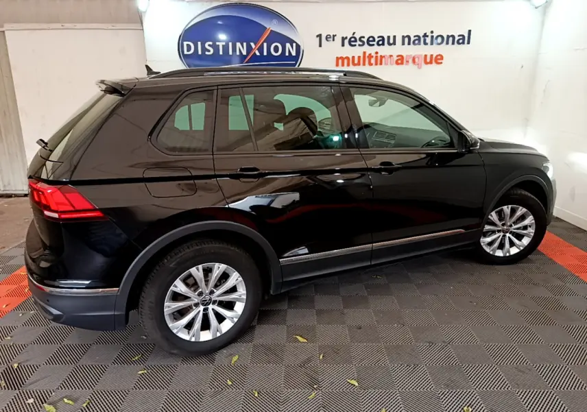 Volkswagen Tiguan noir 2021 vu de profil côté gauche, avec jantes alliage et toit noir brillant en intérieur showroom.