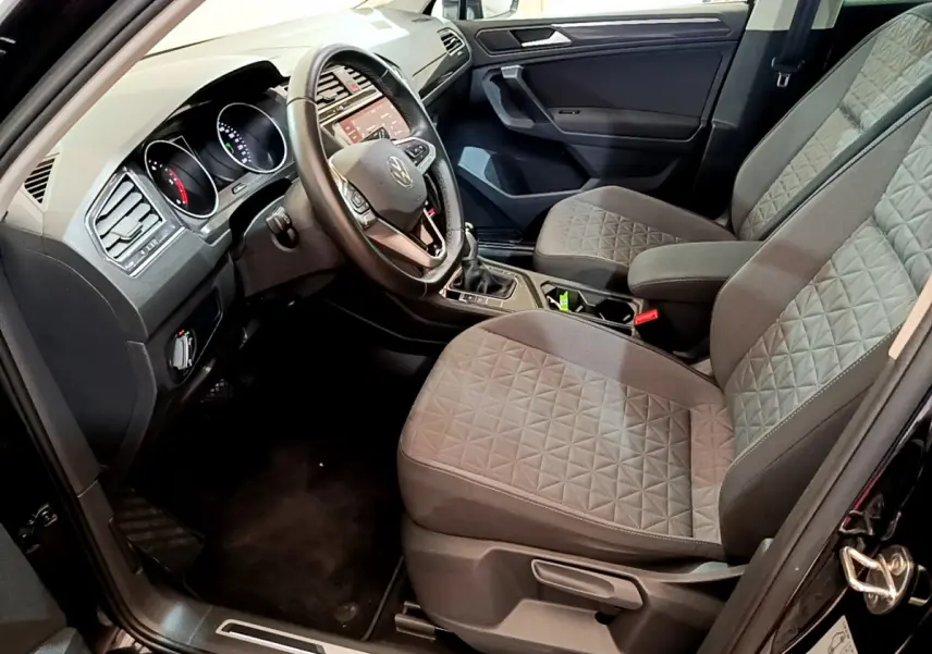 Intérieur avant droit du Volkswagen Tiguan noir 2021, sièges gris à motifs, volant cuir et tableau de bord tactile.