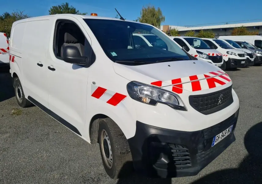 Vue 3/4 avant d'un Peugeot Expert Fourgon blanc avec bandes rouges réfléchissantes et gyrophare orange sur le toit.