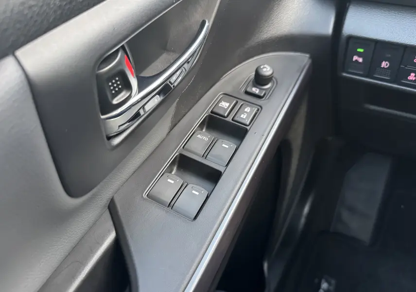 Gros plan sur la commande des vitres et la poignée intérieure côté conducteur du Suzuki S-Cross 2023, finition noire.