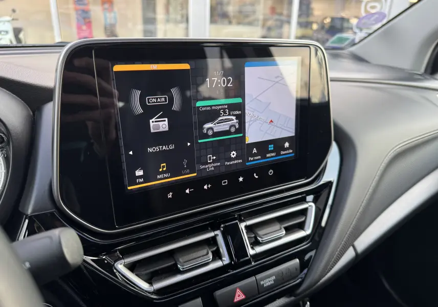 Écran tactile central du tableau de bord du Suzuki S-Cross blanc 2023 affichant radio, consommation et navigation.