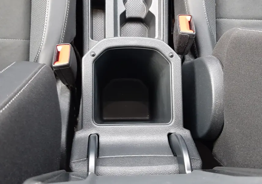 Vue plongeante sur l'accoudoir central noir et la console entre les sièges avant du Volkswagen T-Roc gris Pyrite 2023.