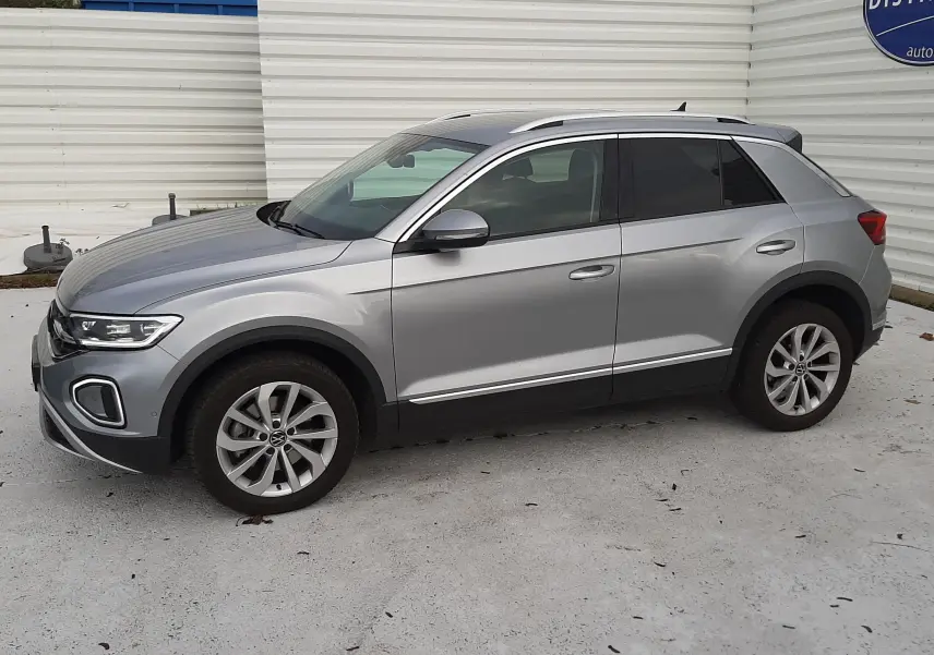 Volkswagen T-Roc gris pyrite en 3/4 avant droit, avec calandre distinctive et feux LED allumés.