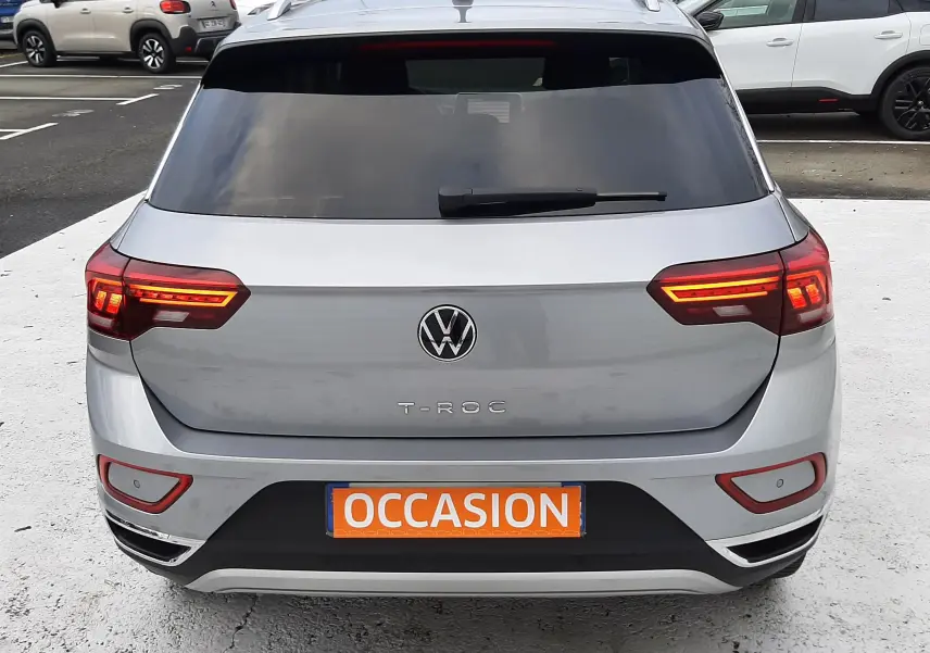 Vue 3/4 arrière droite d'un Volkswagen T-Roc gris pyrite avec vitres arrière surteintées et plaque "OCCASION".