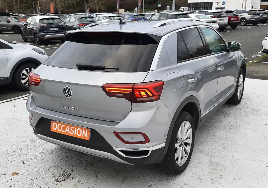 Vue arrière d'un Volkswagen T-Roc gris pyrite 2023 avec feux LED allumés et plaque "OCCASION" orange.