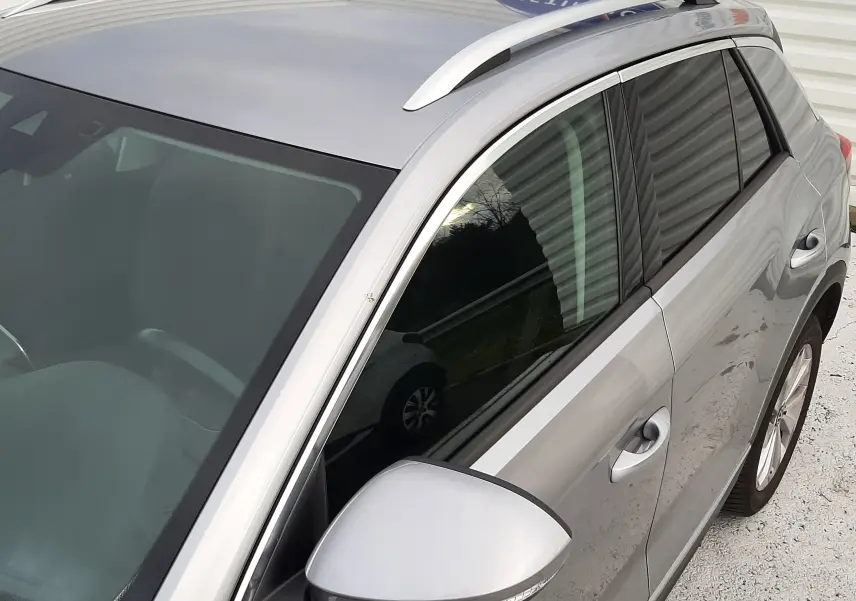 Vue de profil côté gauche d'un Volkswagen T-Roc gris pyrite avec vitres arrière surteintées, stationné sur sol clair.