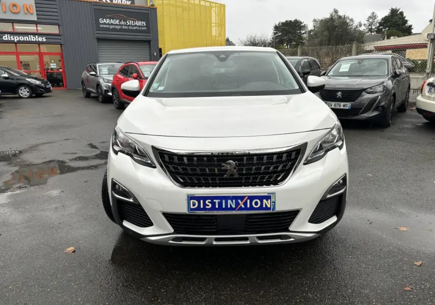 Vue frontale d'un Peugeot 3008 blanc nacré avec calandre noire et plaque Distinxion sur un parking humide.