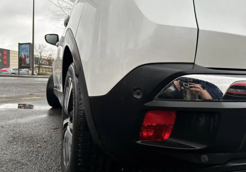 Vue arrière côté gauche d'un Peugeot 3008 blanc nacré avec feu arrière rouge et jante noire sur route humide.