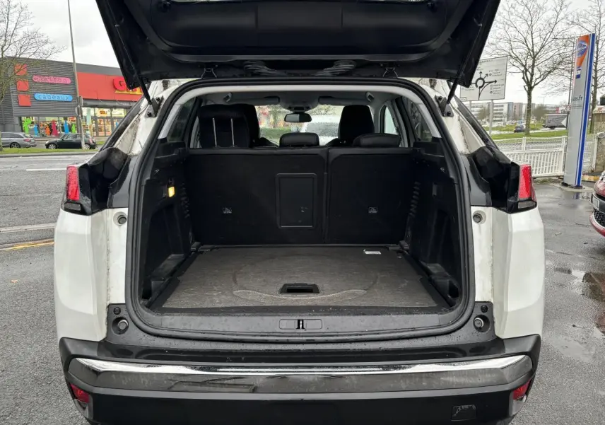 Coffre ouvert d'un Peugeot 3008 blanc nacré vu de l'arrière, montrant l'espace de chargement et les sièges arrière noirs.