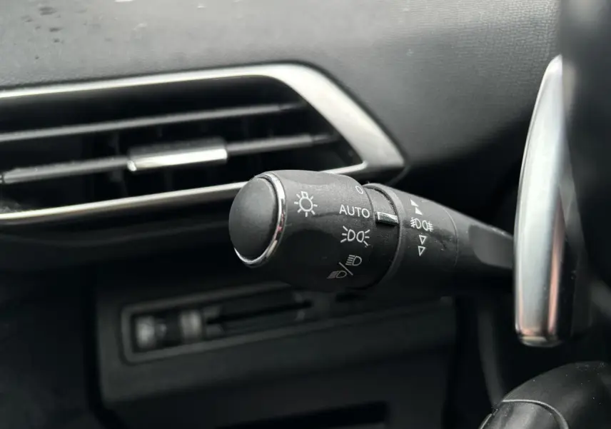 Gros plan sur la commande des feux au volant d'un Peugeot 3008 blanc, intérieur noir avec aérateur argenté.