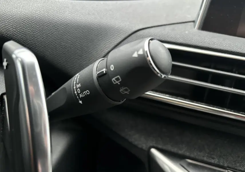 Gros plan sur la commande d’essuie-glace à gauche du volant dans l’habitacle du Peugeot 3008 blanc de 2018.
