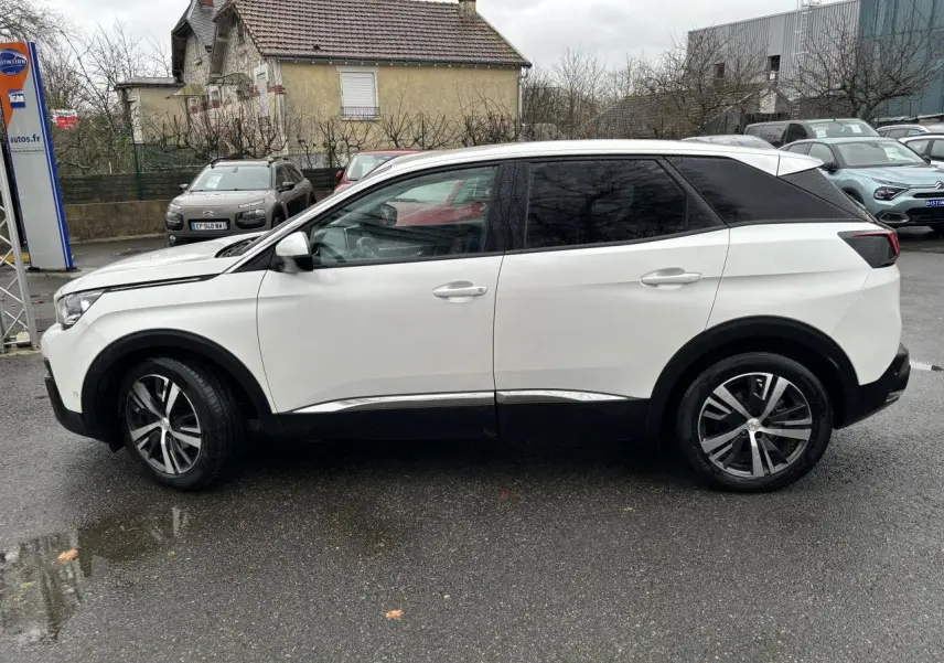 Profil côté gauche du Peugeot 3008 blanc nacré de 2018 avec toit noir et jantes alliage bicolores sur parking humide.