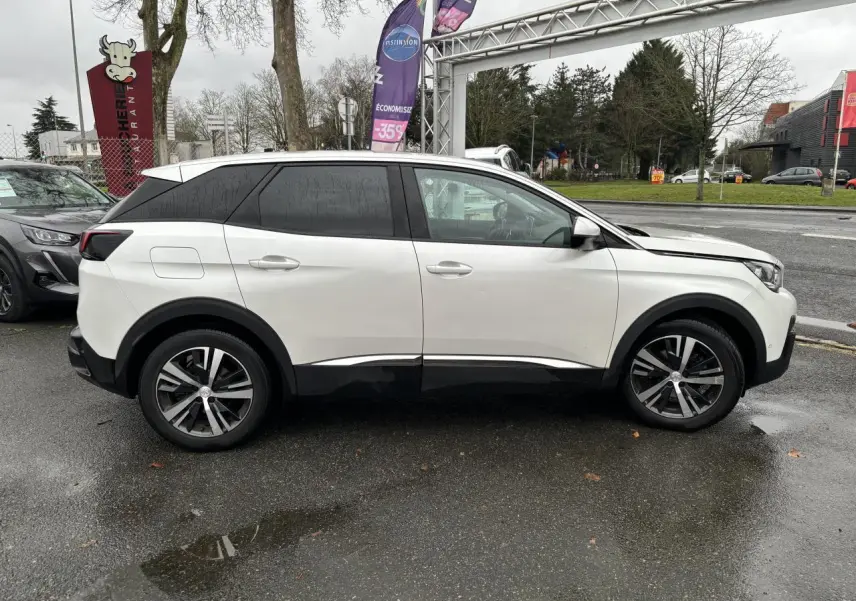 Profil côté gauche d'un Peugeot 3008 blanc nacré avec toit noir et jantes alliage sur un parking extérieur.