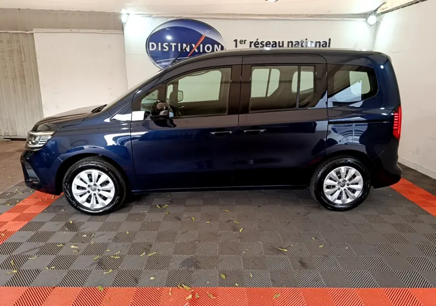 Profil latéral gauche d'un Renault Kangoo bleu 2023 dans un showroom avec jantes argentées et vitres teintées.