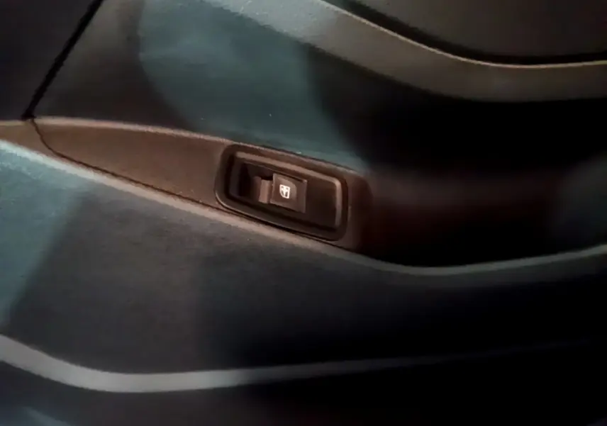 Gros plan sur l'interrupteur de lève-vitre intégré à la garniture intérieure noire d'une Renault Kangoo bleu 2023.