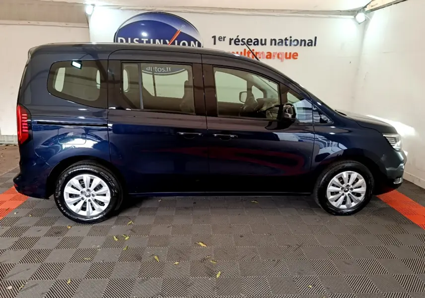 Profil côté droit d'un Renault Kangoo bleu 2023 garé en intérieur sur sol à damiers noirs et rouges.