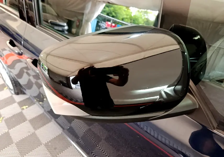 Rétroviseur droit noir brillant sur Renault Kangoo bleu, reflet de l'environnement intérieur du garage.