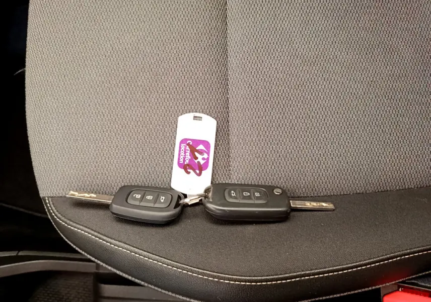 Gros plan sur deux clés Renault noires posées sur un siège tissu gris foncé à coutures blanches.