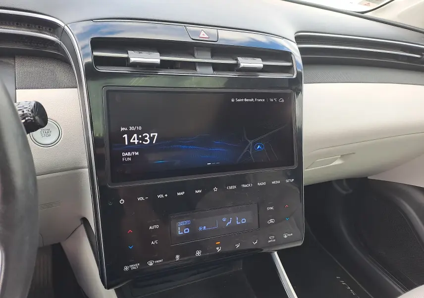 Tableau de bord beige du Hyundai Tucson 2023 avec écran tactile central et bouton start/stop visible côté gauche.