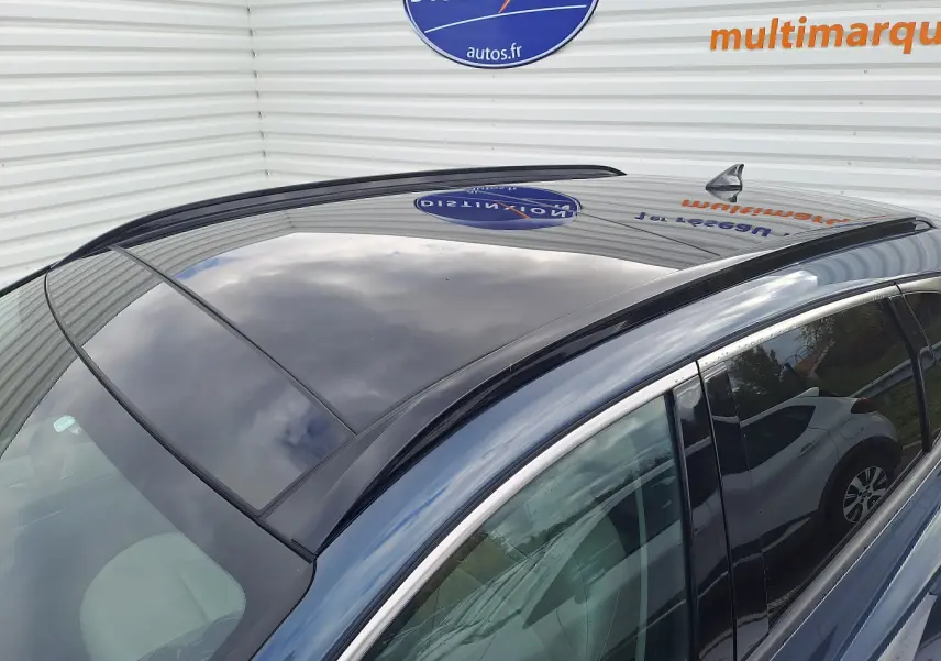 Toit panoramique en verre noir du Hyundai Tucson Cypress Green vu de dessus côté droit, reflet du ciel et panneau mural visible.