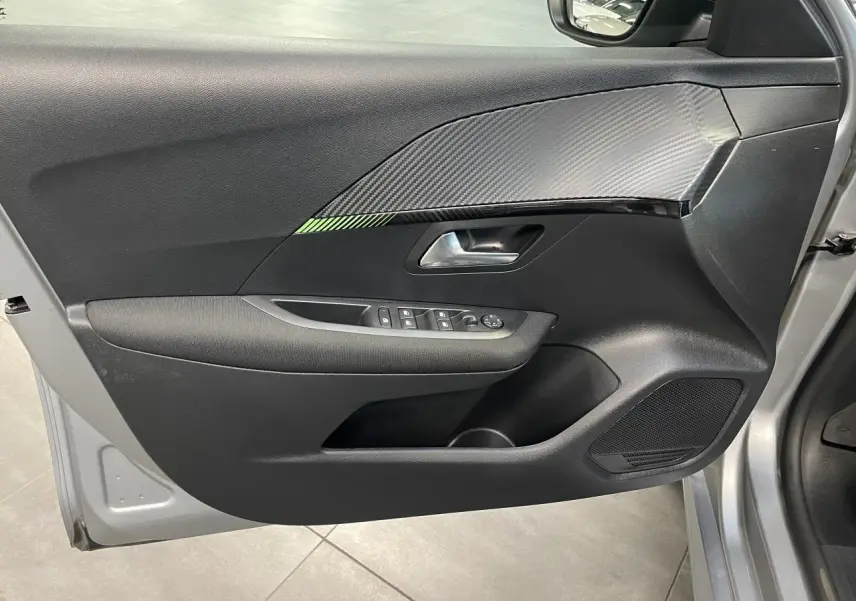 Vue rapprochée de la porte avant gauche gris clair du Peugeot 208 avec insert décor carbone et commandes électriques.