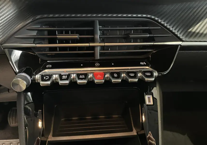 Vue rapprochée de la console centrale noire brillante avec commandes tactiles et boutons métallisés du Peugeot 208 gris clair 2024.